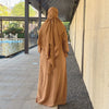 A full-length, flowing camel-colored abaya and khimar set displayed outdoors on a paved walkway.
