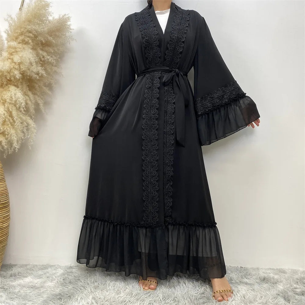 Eine Frau modelliert eine elegante schwarze, bodenlange Abaya mit Spitzenbesatz und mehrreihigem Rüschensaum.