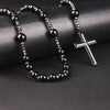 Pendentif de croix en hématite noire avec petites perles sombres et un charm de croix en argent sur une surface sombre.