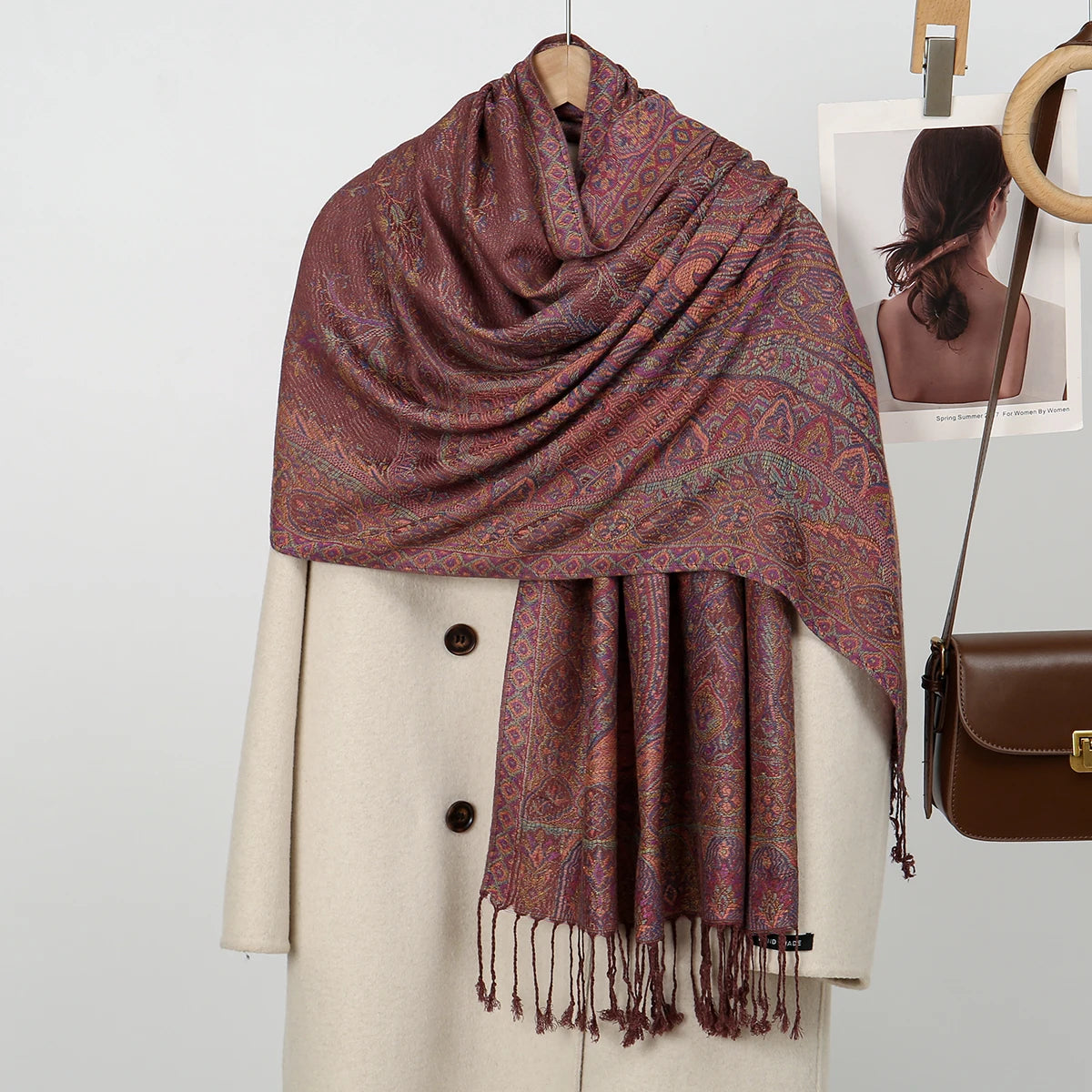 Una estola bordada de paisley marrón y púrpura drapeada alrededor del cuello de una modelo, combinada con un abrigo beige.