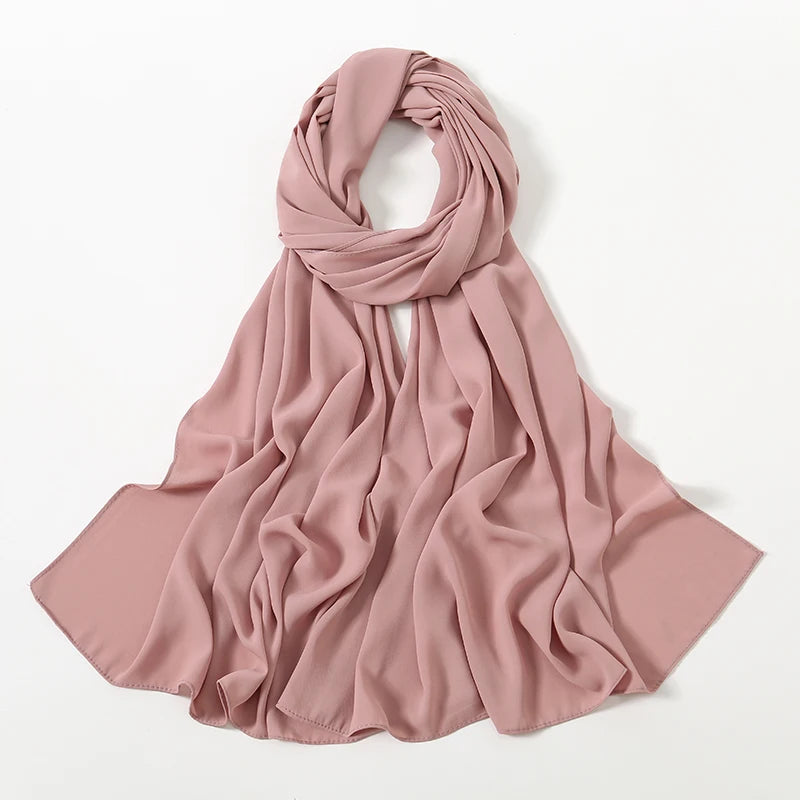 Fließender, staubrosa Chiffon-Schal, zu einem weichen Knoten gebunden und auf weißem Hintergrund ausgebreitet.