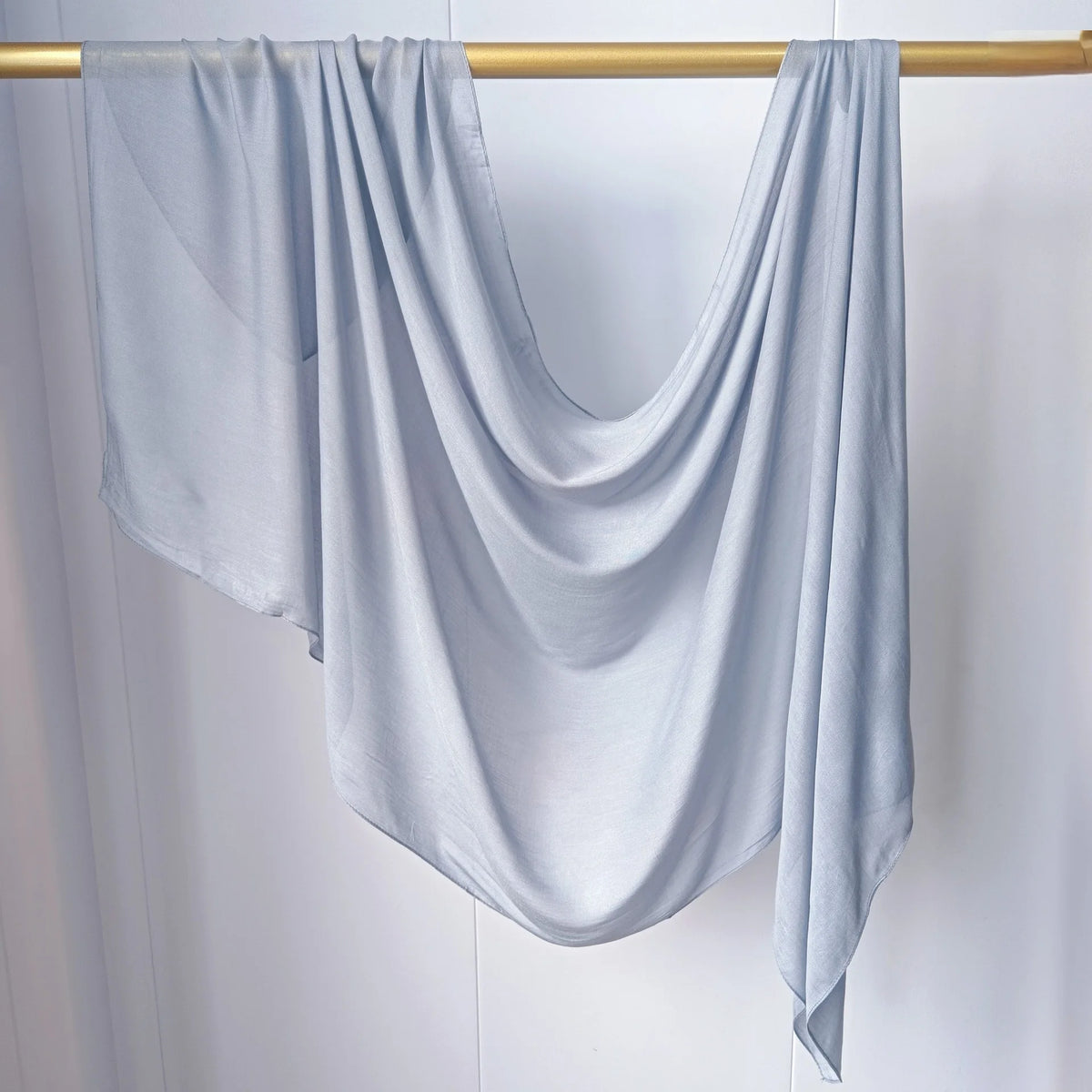 Foulard hijab uni bleu clair drapé sur un bâton en bois.