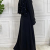 Eine Frau trägt eine elegante schwarze Maxi-Abaya mit durchscheinenden Ärmeln vor einer weißen Paneelwand.