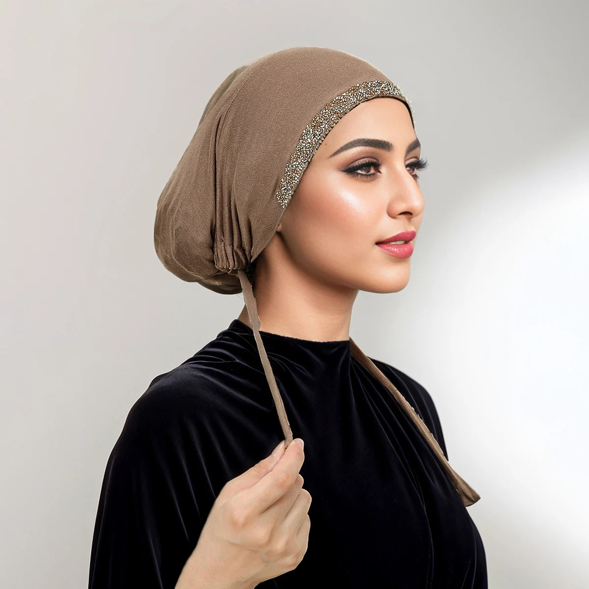 Eine Frau trägt einen beige Hijab mit Strassbesatz und ein schwarzes Samt-Oberteil.