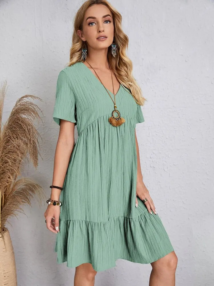 Eine Frau modelliert ein elegantes mintgrünes V-Ausschnitt Minikleid mit goldenen Frangenschmuck und Armreifen.