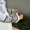 Gros plan d'une abaya blanche avec broderies noires et bordure de dentelle portée par une femme.