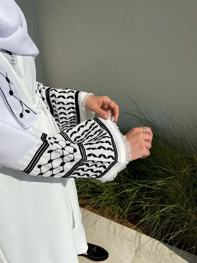 Gros plan d'une abaya blanche avec broderies noires et bordure de dentelle portée par une femme.