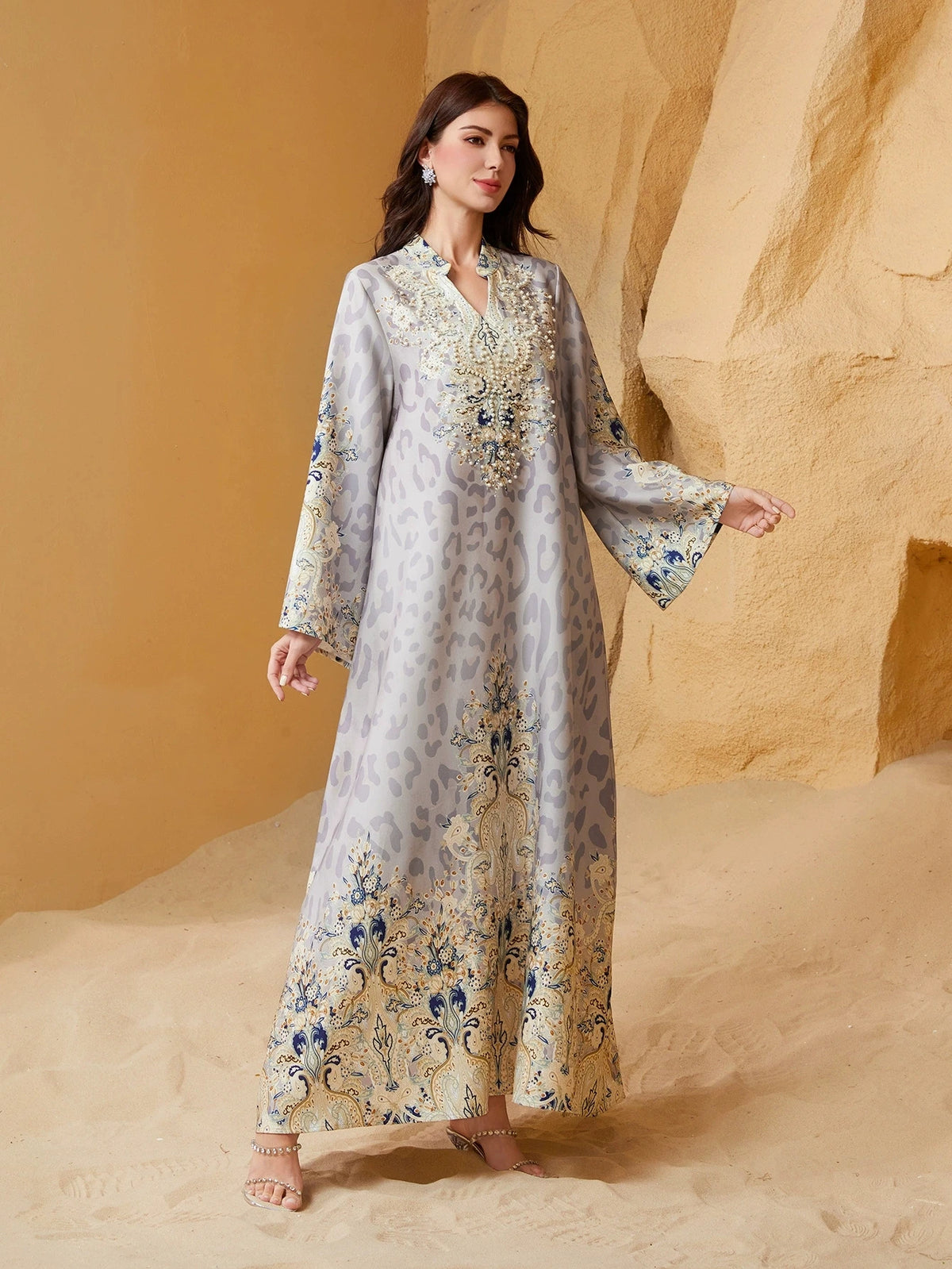 Una mujer vistiendo una abaya larga y fluida de leopardo beige y azul con adornos de diamante, de pie en un entorno desértico