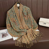 Pañuelo pashmina de lujo en tonos verde oliva y marrón estampado, drapeado sobre una superficie de cuero marrón.