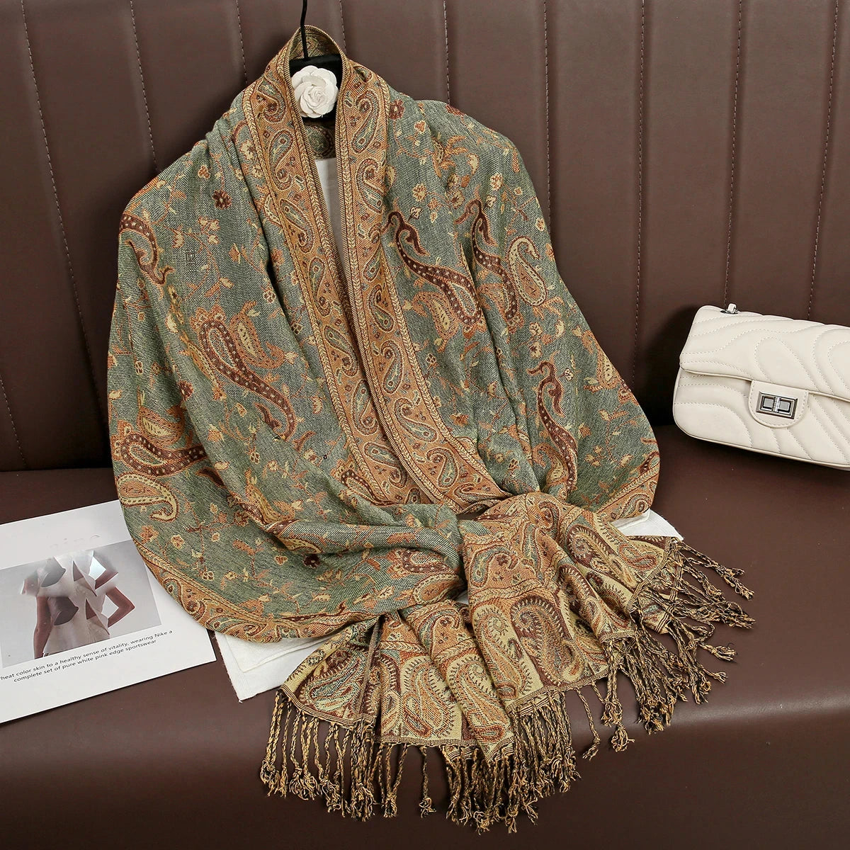 Pañuelo pashmina de lujo en tonos verde oliva y marrón estampado, drapeado sobre una superficie de cuero marrón.