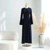 Una elegante abaya de manga larga azul marino, exhibida en un maniquí junto a hierba pampas beige seca y un sofá blanco.