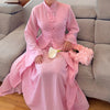 A woman wearing an elegant pink two-piece Arabic modest set with flowing fabric sitting on a gray sofa.
