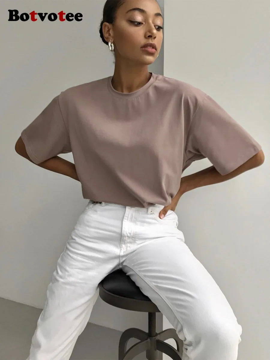 Una mujer modela una camiseta básica oversize de algodón beige y pantalones blancos.