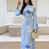 Eine Frau modelliert ein hellblaues Abaya-Kleid mit aquarelligen Blumenakzenten in einem hellen Innenraum.