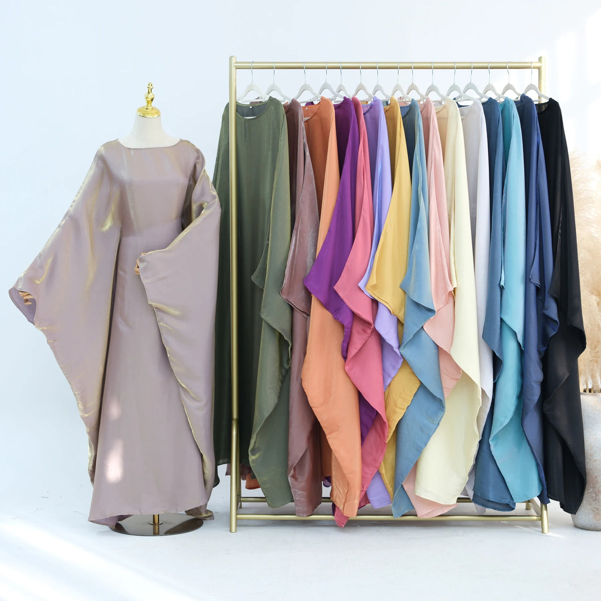 Eine Reihe eleganter Kaftan-Kleider in verschiedenen Pastell- und Erdtönen, aufgehängt an einem goldfarbenen Haken.