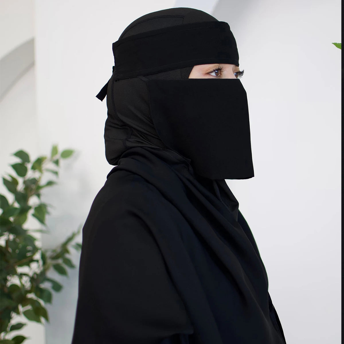 Eine Frau mit schwarzem, atmungsaktivem Mesh-Hijab und Halsband, Profilansicht.