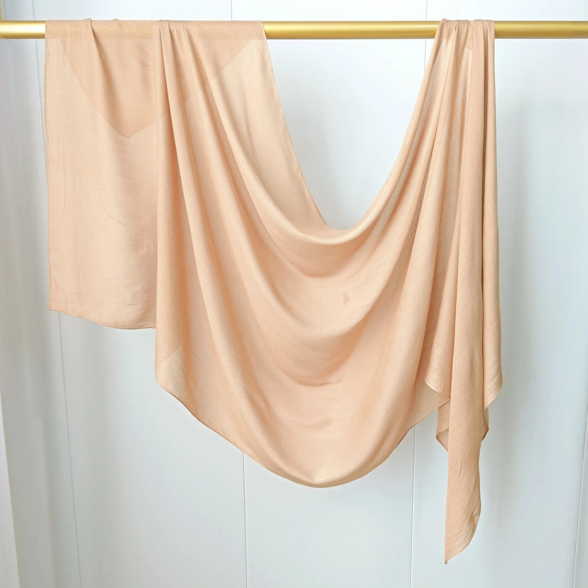Un foulard modal beige uni et fluide drapé sur un cintre or contre un fond blanc.