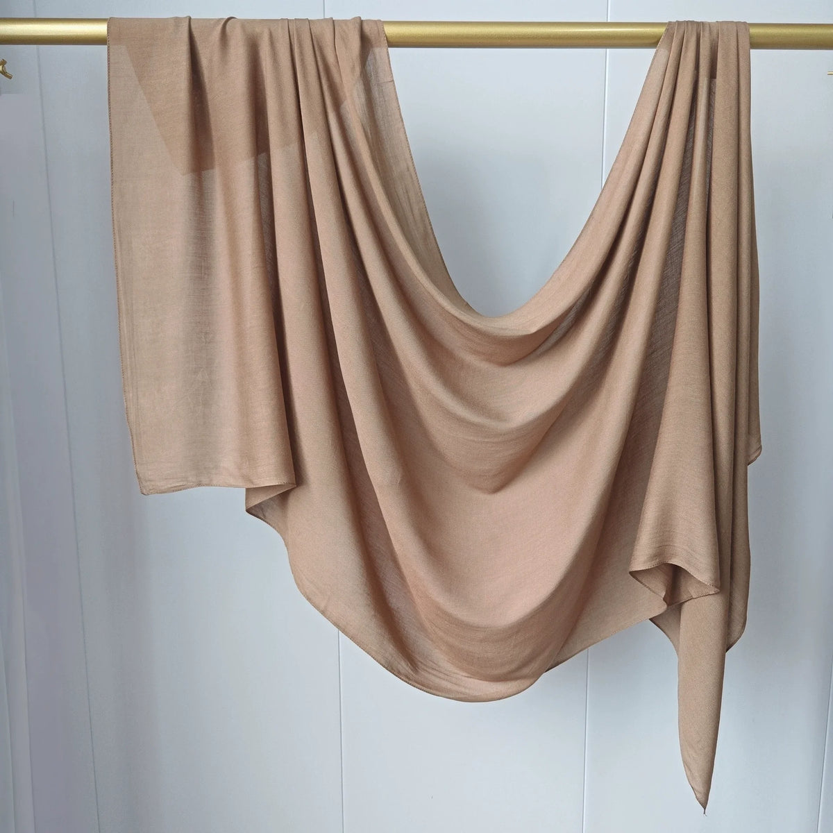 Écharpe de hijab couleur beige unie drapée sur un cintre en bois.