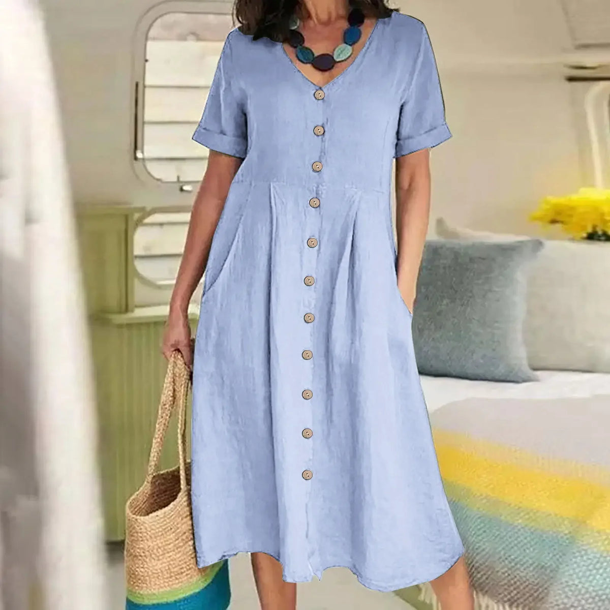 Eine Frau trägt ein hellblaues Baumwoll- und Hanf-V-Ausschnittkleid mit kurzen Ärmeln und gerafftem Rock.
