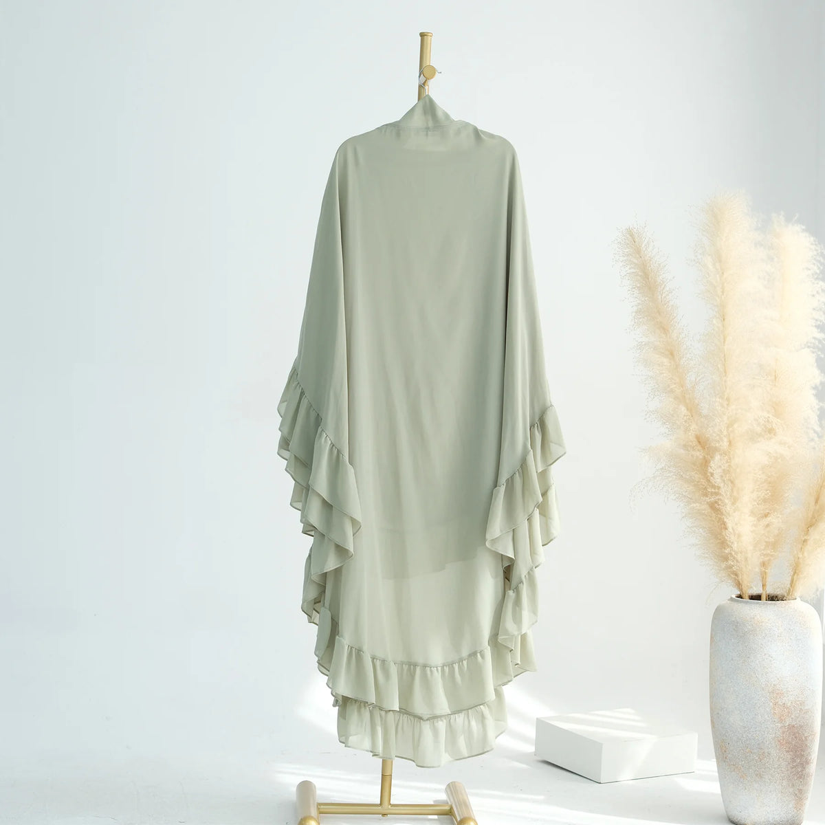 A sheer sage green ruffled two-layer chiffon hijab displayed on a wooden hanger.