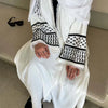 Une femme portant une abaya musulmane blanche brodée avec des bordures noires et des chaussures noires.