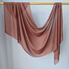 Un foulard modal transparent de couleur terracotta flottant, drapé sur un cintre doré contre un mur blanc.