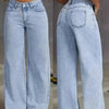Una mujer modela pantalones vaqueros anchos azul claro con un top blanco corto.