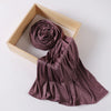 A mauve ribbed jersey hijab scarf is rolled and draped within a light wooden frame.