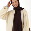 Eine Frau trägt einen dunkelbraunen Chiffon-Hijab und einen cremefarbenen Strickpullover.