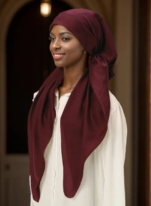 Una mujer vistiendo un hiyab borgoña intenso y una blusa crema, sonriendo ligeramente.