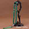 A dark wooden stand holds a necklace of green beads and a tassel.