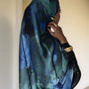 Une femme portant un foulard hijab en satin de soie imprimé bleu et vert, vue de profil.