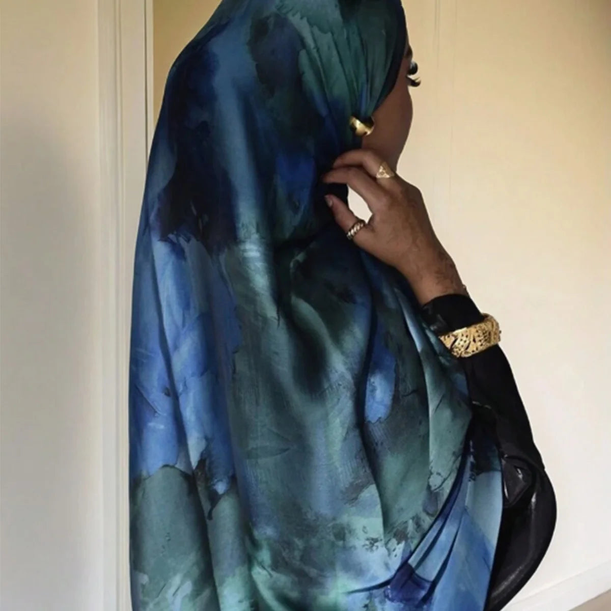 Une femme portant un foulard hijab en satin de soie imprimé bleu et vert, vue de profil.