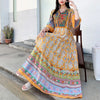 Eine Frau modelliert ein langes, fließendes Boho-besticktes Maxi-Kleid in Gelb- und Orangetönen mit farbigem Zierrand.
