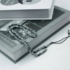 A string of dark gray beads used as an Islamic prayer tasbih for meditation and prayer resting on a book.