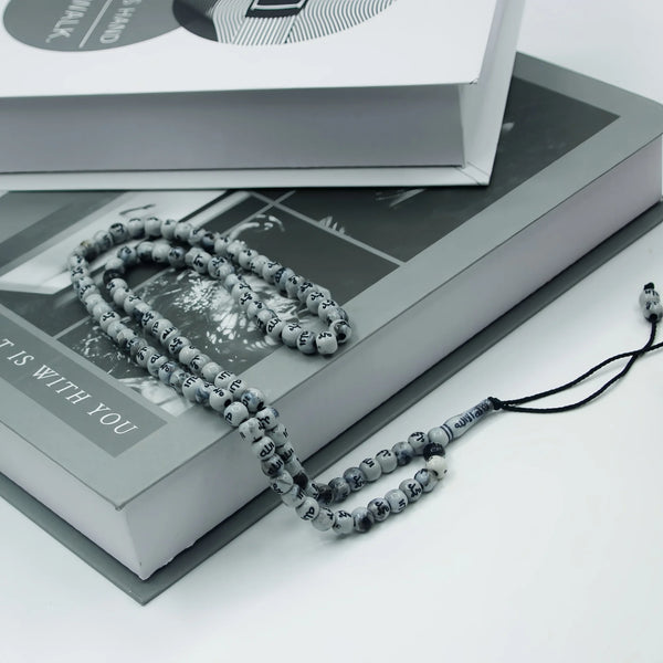 A string of dark gray beads used as an Islamic prayer tasbih for meditation and prayer resting on a book.