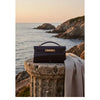A black crocodile pattern shoulder bag resting on a stone pedestal by the sea.