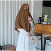 Eine Frau in brachem Hijab und weißem Kleid wird drinnen gezeigt.