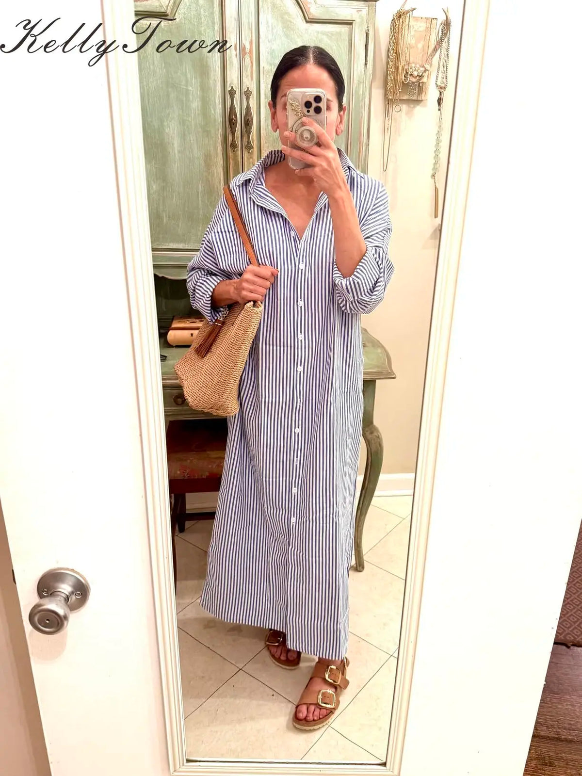 Eine Frau in einem langen, gestreiften Baumwollmaxi-Kleid mit Knopflevers und lockerem Schnitt vor einem Spiegel.