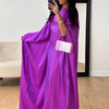 Una mujer modela una vibrante abaya de satén morado batwing con una pulsera dorada y un bolso transparente.