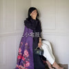 Una mujer vistiendo un cárdigan abaya plisado negro con bufanda floral morada, posando en interiores.
