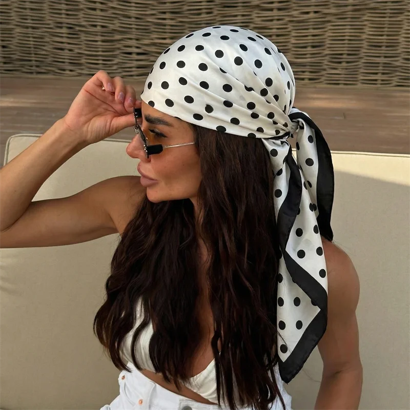 A woman wearing an elegant silk dot print scarf tied around her hair and neck.