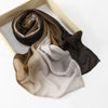 Stapel von Aquarelldrucken aus Baumwolle und Modal-Hijabs in Braun-, Beige- und Grautönen, präsentiert in einer Holzkiste.