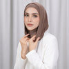 Une femme portant un bonnet hijab double couche marron et un haut blanc, regardant directement l'appareil photo.
