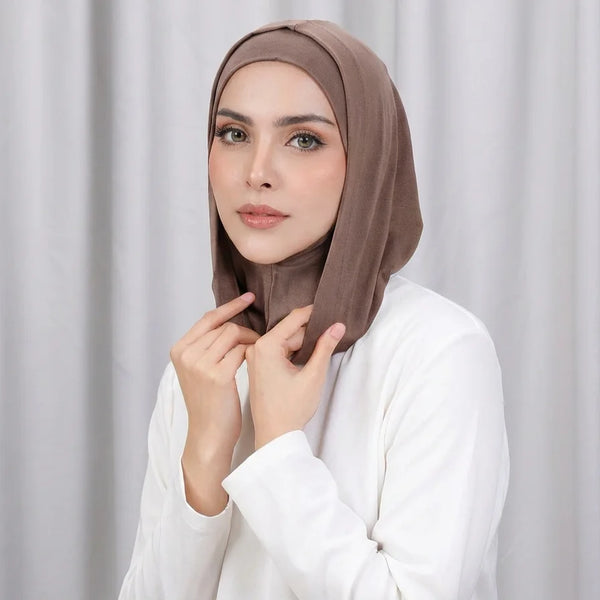 A woman wearing a brown instant double layer hijab cap and white top, looking directly at the camera.
