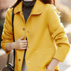 Une femme portant un manteau en laine jaune vif sur un col roulé gris et un pantalon clair.
