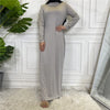 Eine Frau in einem eleganten grauen Rollkragen-Maxi-Abaya-Kleid vor einer weißen Paneelwand.
