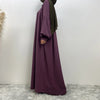 Eine Frau trägt ein elegantes langes lila islamisches Kleid mit einem dunkelgrünen Hijab.