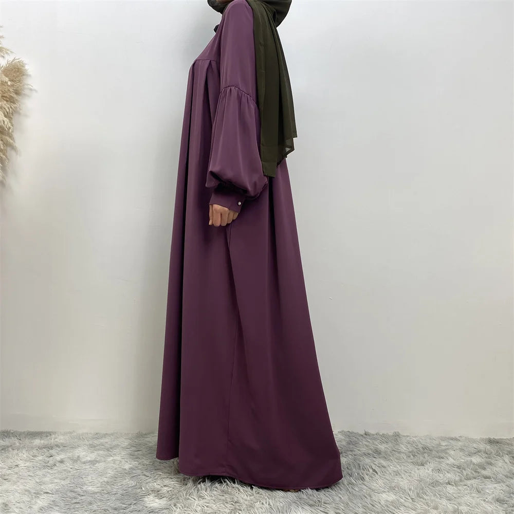 Eine Frau trägt ein elegantes langes lila islamisches Kleid mit einem dunkelgrünen Hijab.
