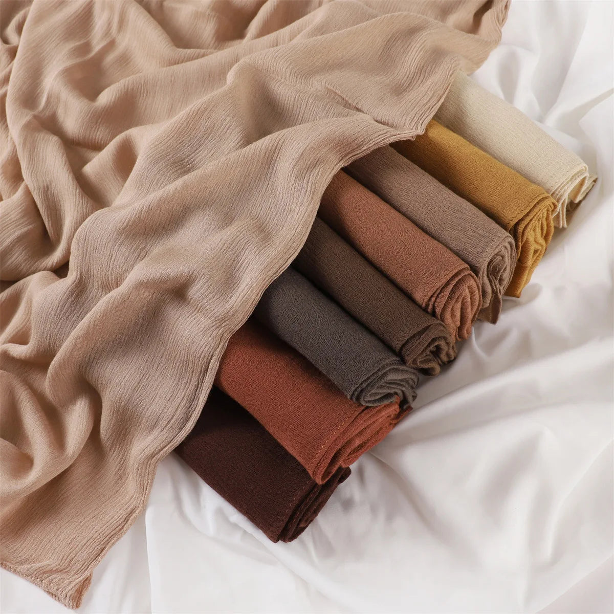Pile de foulards ou châles en crêpe de rayon aux tons terreux : beige, olive et rouille.